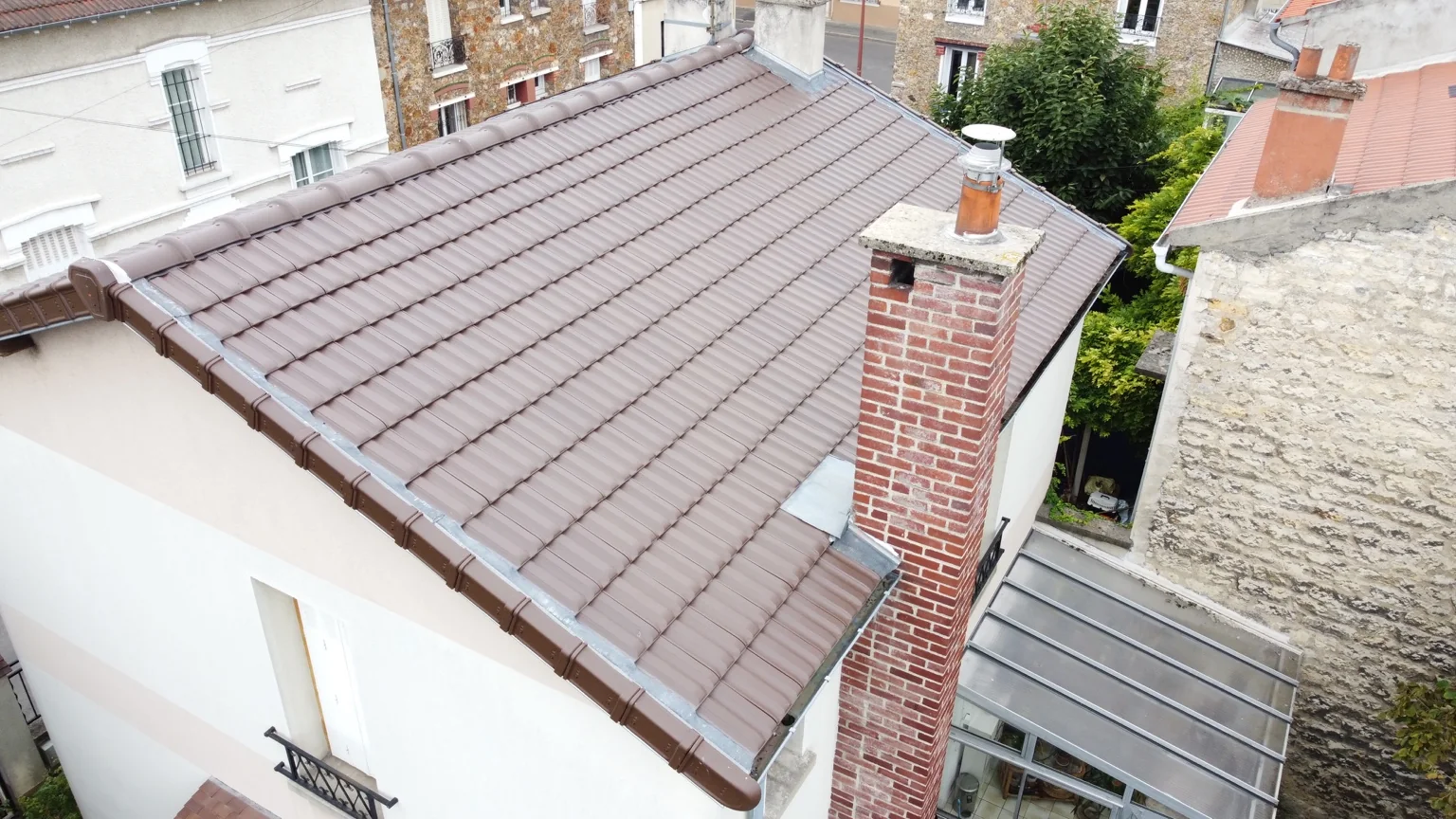 Autre versant de la toiture en tuiles avec une grande cheminée en brique et une véranda dans l’Oise