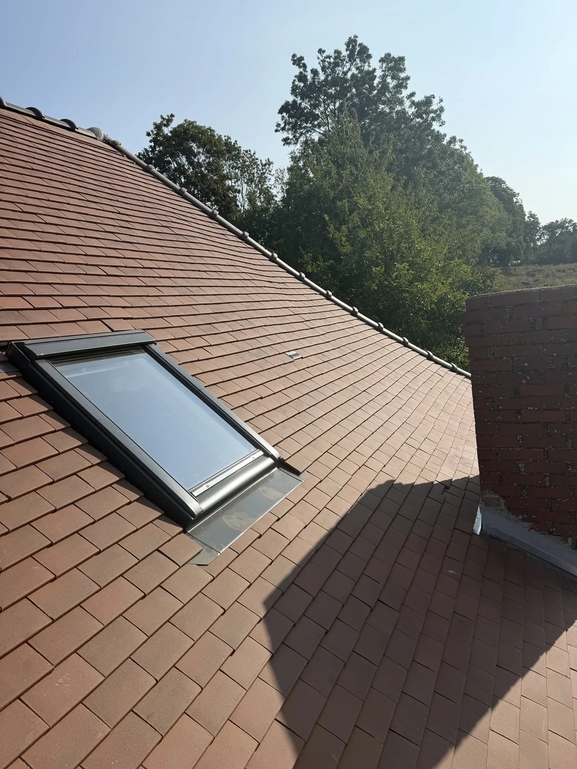 Détail après rénovation aux alentours de Beauvais montrant une fenêtre de toit, la couverture rouge et le raccord de cheminée