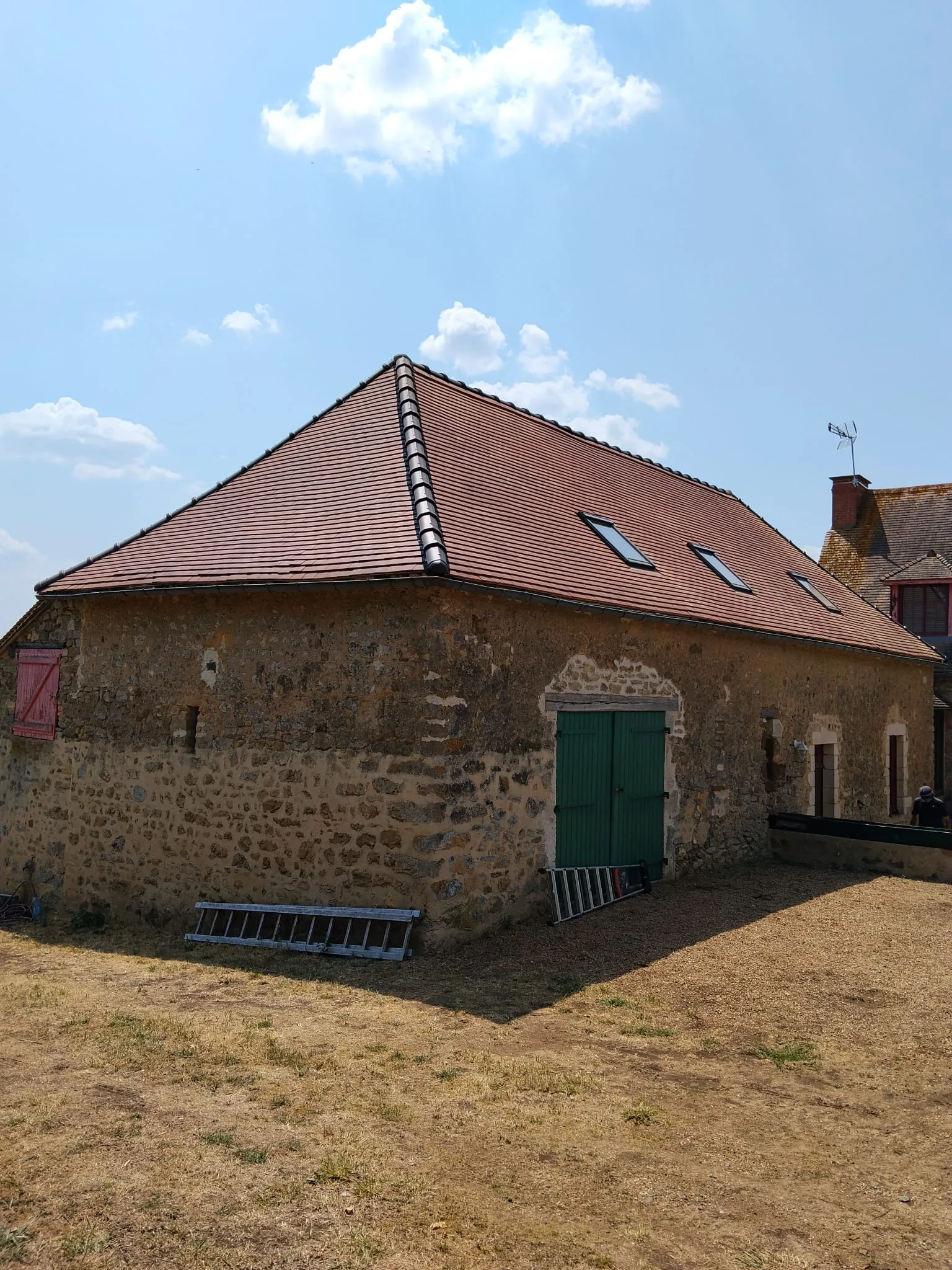 Bâtisse en pierre aux alentours de Beauvais après rénovation, avec couverture rouge régulière, fenêtres de toit et porte verte