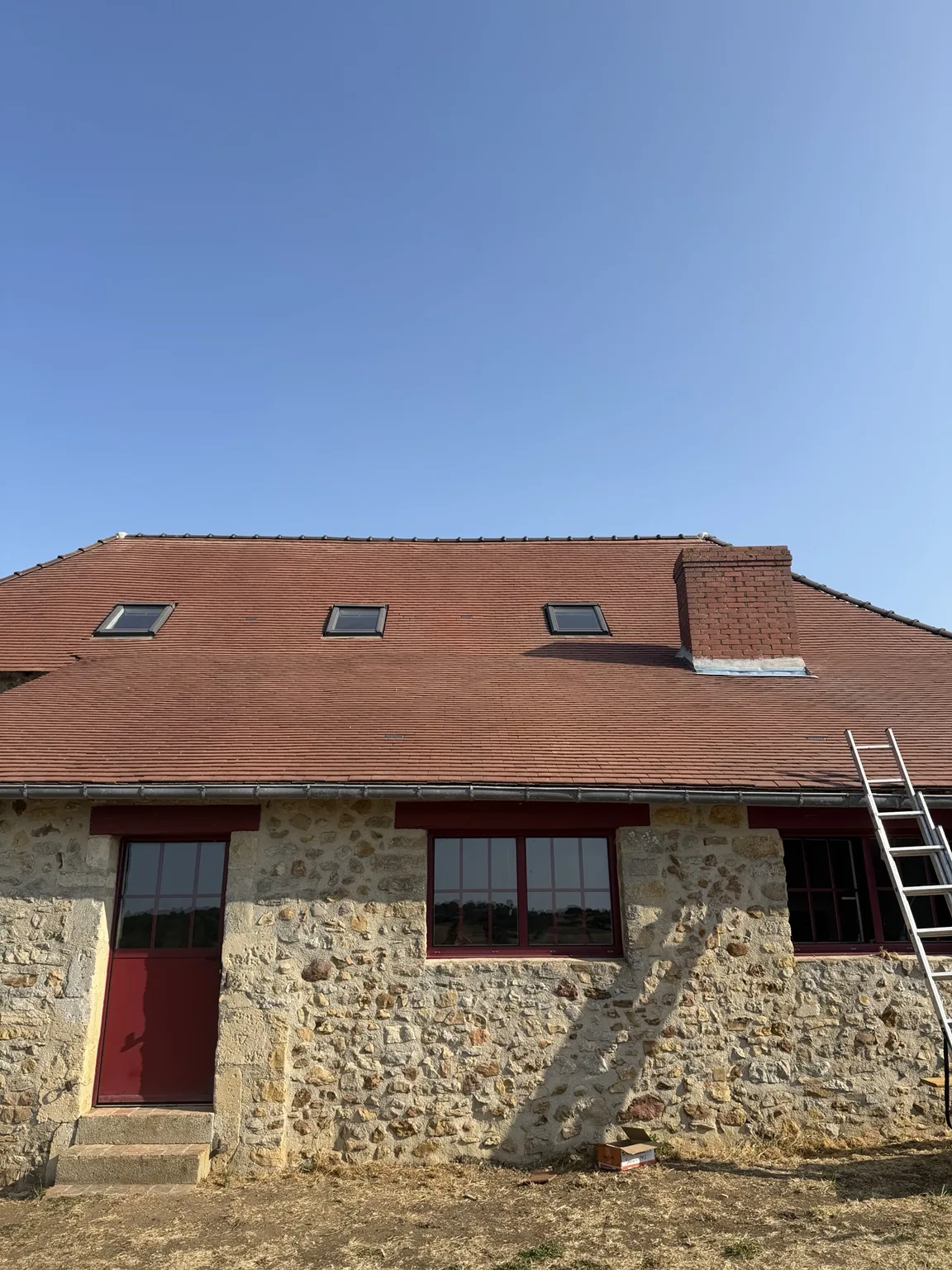 Versant après rénovation aux alentours de Beauvais, avec couverture rouge, cheminée en brique, menuiseries rouges et fenêtres de toit