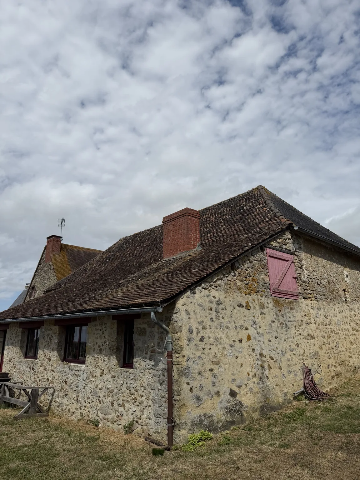 Versant de toiture ancien avant rénovation aux alentours de Beauvais, avec cheminée en brique et volet rose