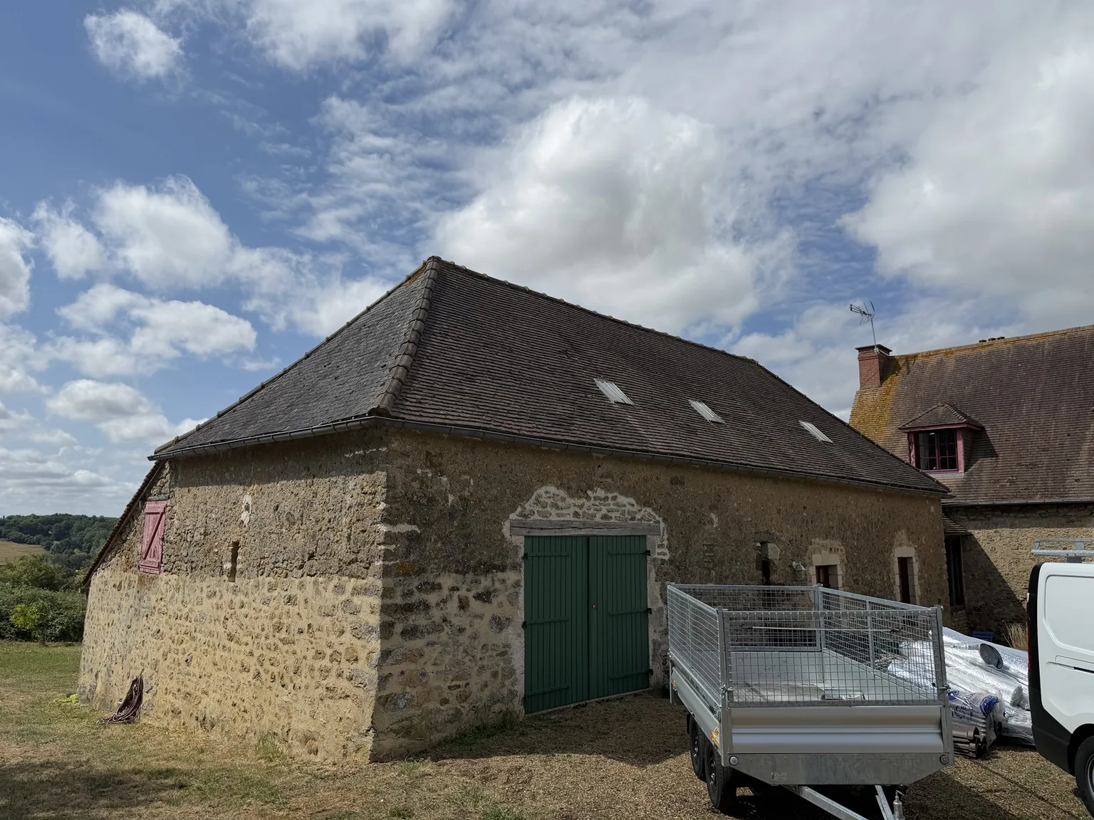 Bâtisse en pierre aux alentours de Beauvais avant rénovation, avec porte verte, toiture ancienne sombre et remorque